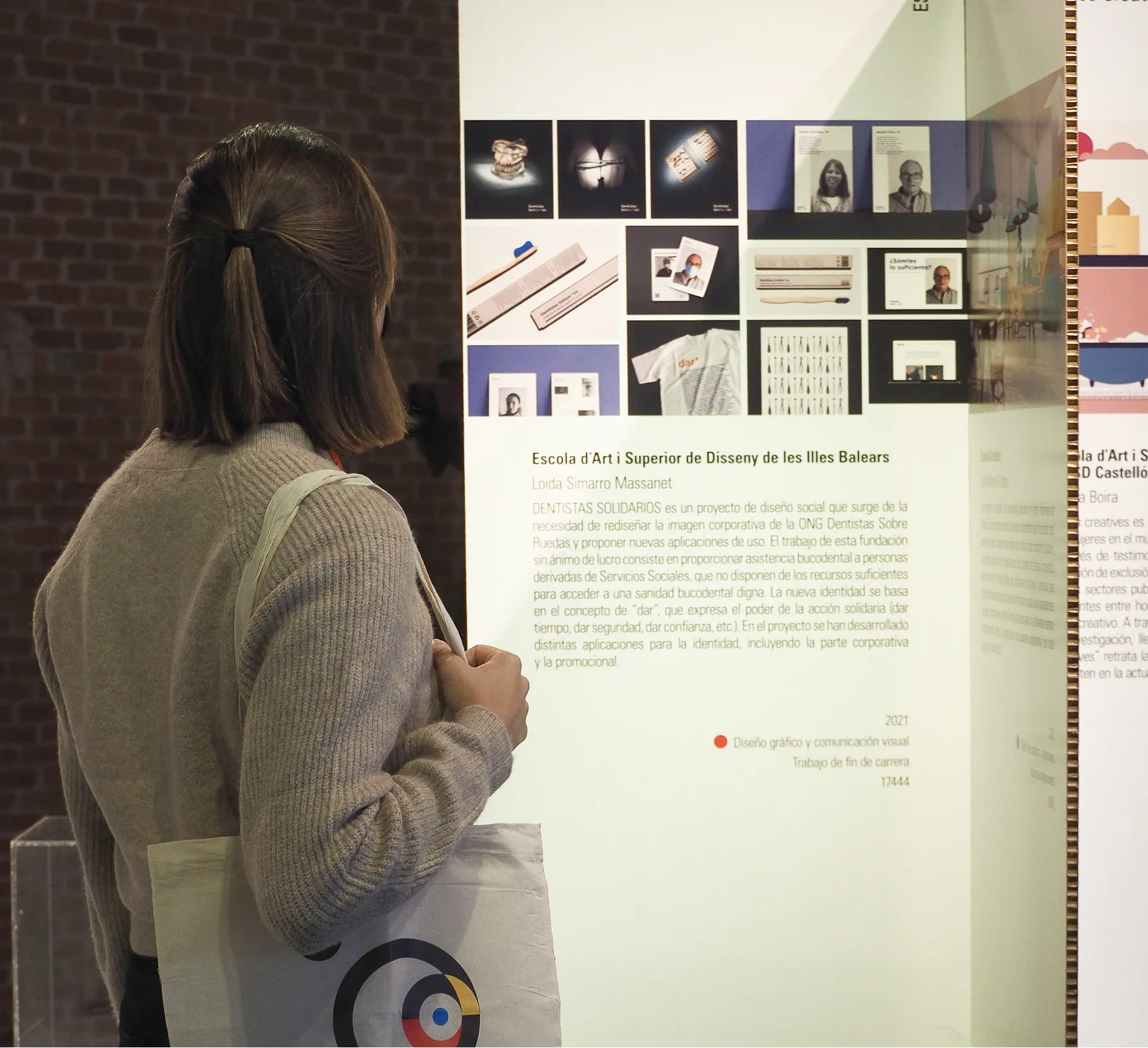 Loida Simarro carrying a "9º Encuentro Bienal Iberoamericana de Diseño - Enseñanza y Diseño" tote bag while observing the "Dentistas Solidarios" project exposition.